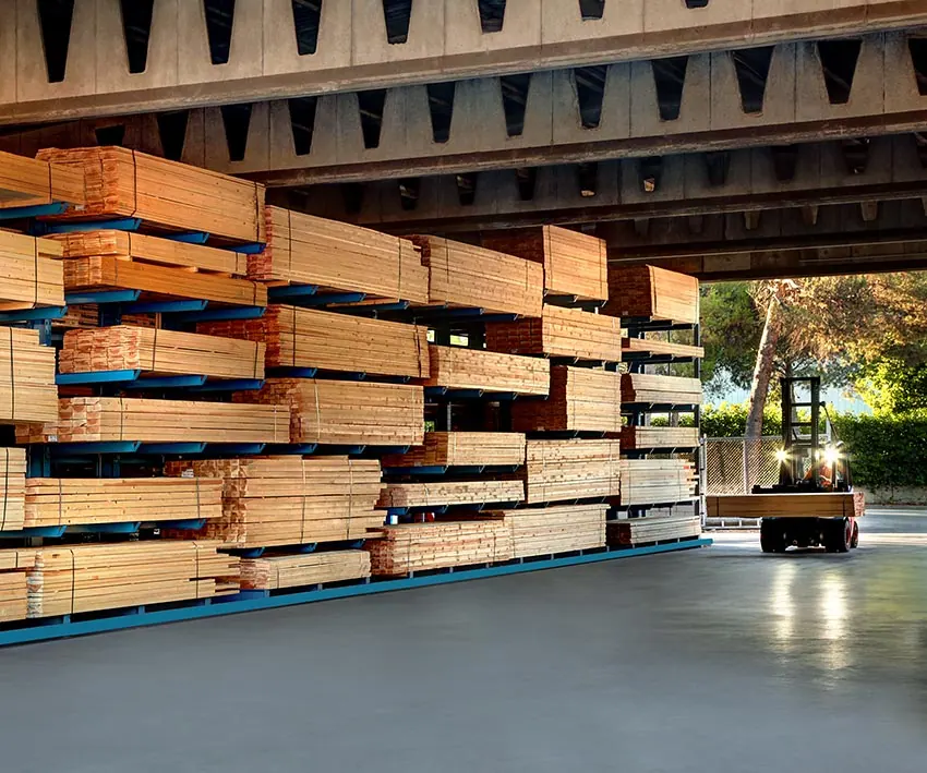 Interior de bodega con pilas de tableros y madera y un montacargas